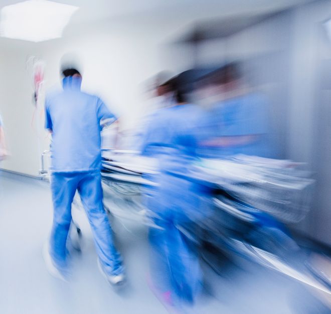A blurry action shot of medical professionals in blue scrubs rushing a patient on a gurney down a hospital hallway